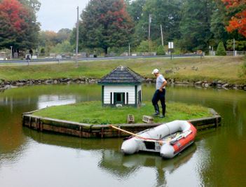 Public Services crew member performing duck house maintenance on an island in the middle of the pond